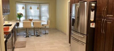 A galley type kitchen with working space and refrigerator on opposite ends. A dining table with white chairs on the background