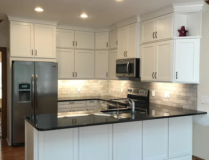 A well-lit kitchen designed for function and style. The white cabinets offer plenty of storage, while the black countertops provide a sleek and durable work surface. Stainless steel appliances and pendant lights add a touch of modern sophistication.